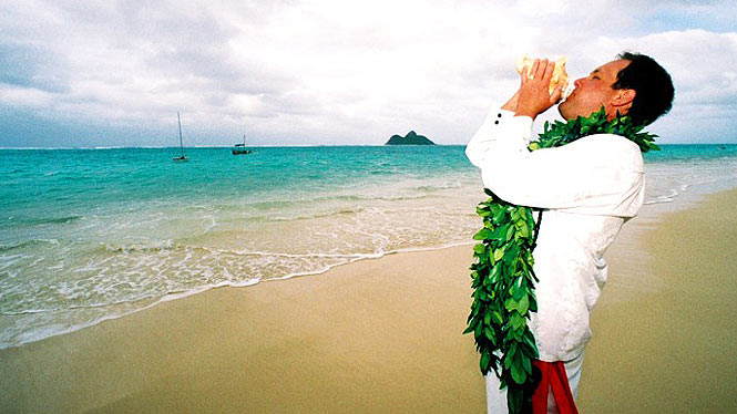 Groom wearing Maile lei and blowing a conch shell